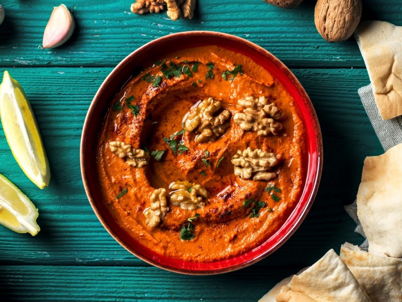 Schale Granatapfel-Paprika-Dip mit Fladenbrot Zitrone und Gewürze daneben.