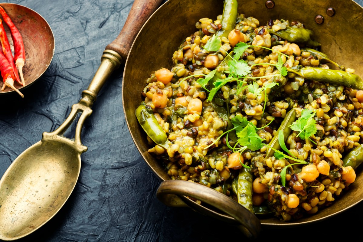 Kitchari, indischer Kokosreis mit Bohnen und Kichererbsen, in einer Blechschüssel, daneben ein Löffel. Draufsicht.