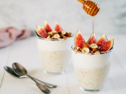 Zwei Gläser Overnight Oats mit Feigen. Über eines davon wird Honig geträufelt.