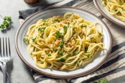 Ein Teller Spaghetti aglio e olio mit Chili und Petersilie, daneben eine Gabel.