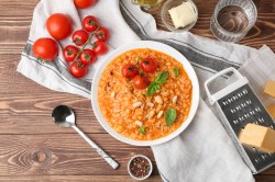 Risotto mit Tomaten auf einem Holztisch, Tomaten und Küchenreibe daneben