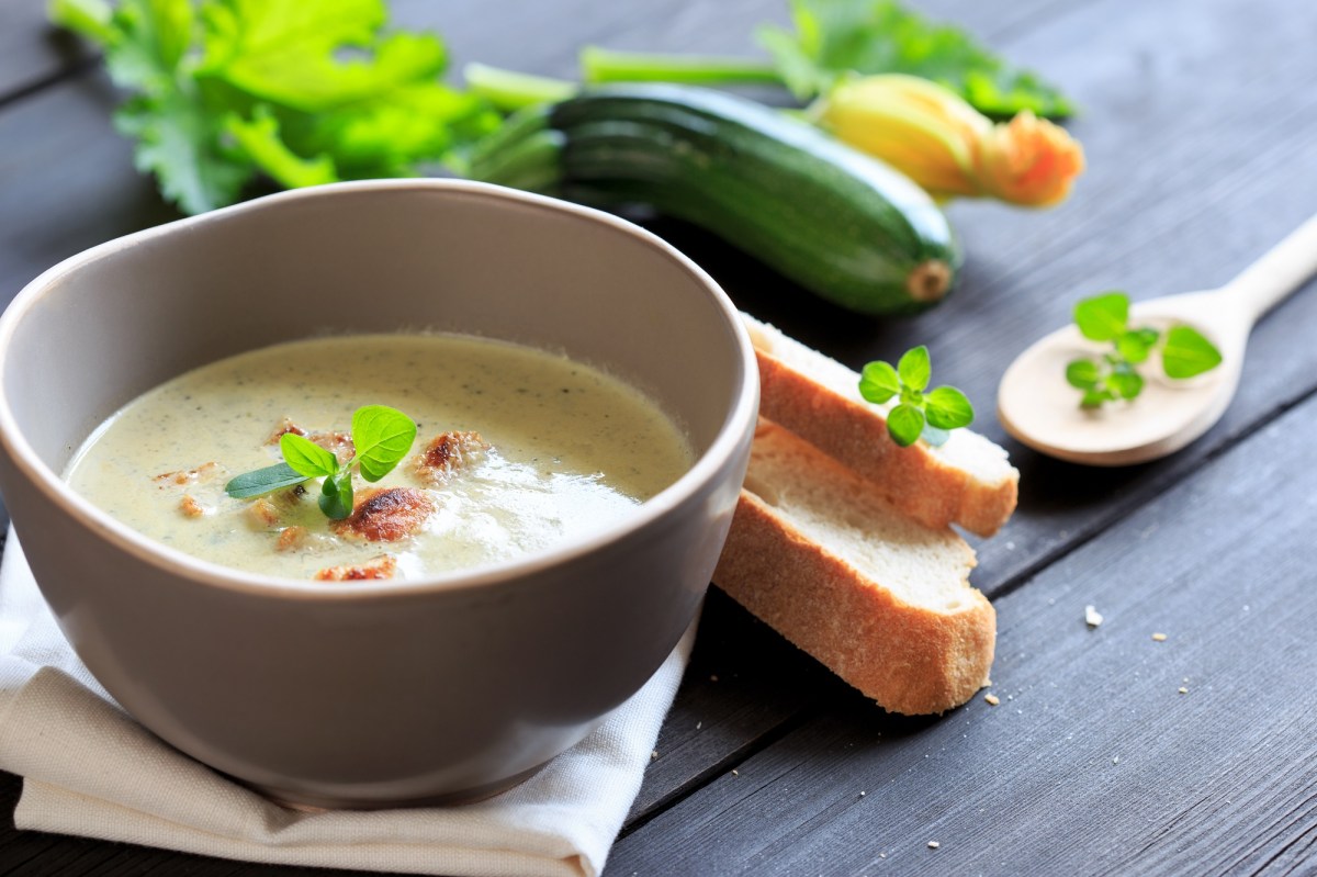 Schale mit Zucchini-Kokos-Suppe und Gemüse daneben