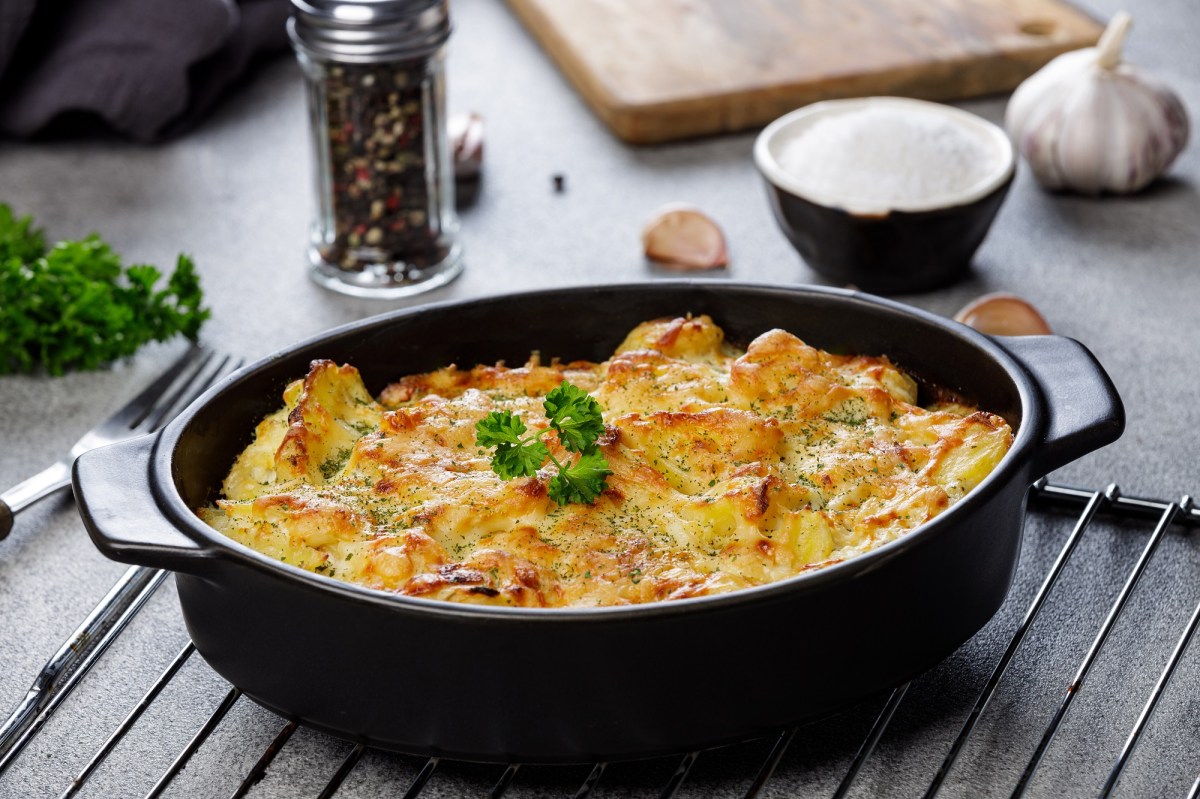 Knoblauch-Kartoffelauflauf in einer dunken ovalen Auflaufform, die auf einem Ofengitter steht.