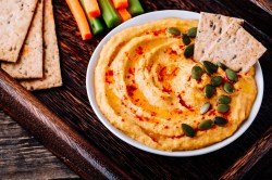 Schale mit Kürbis-Frischkäse-Dip auf Tablett, Cracker und Gemüsesticks