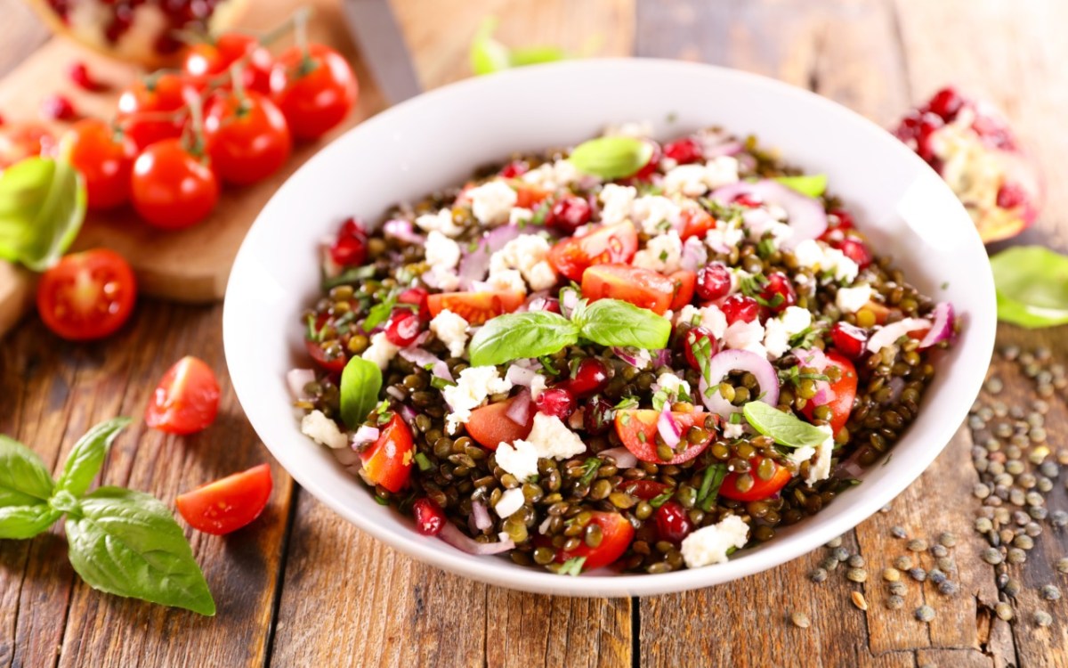 Eine Schüssel Linsensalat mit Feta. Daneben liegen frische Zutaten.