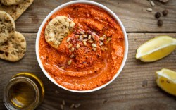 Eine Schale mit Paprika-Tomaten-Hummus. Daneben liegen frische Zutaten.