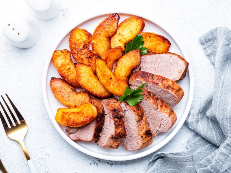 Angeschnittenes Schweinefilet mit geschmorten Ã„pfeln auf einem weiÃŸen Teller.