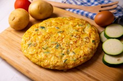 Eine Tortilla de Patata mit Zucchini auf einem Holzbrett.