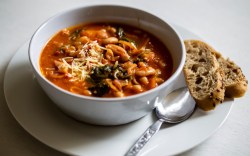 Eine Schüssel mit toskanischer Bohnensuppe. Daneben liegen eine Scheibe Brot und Löffel.