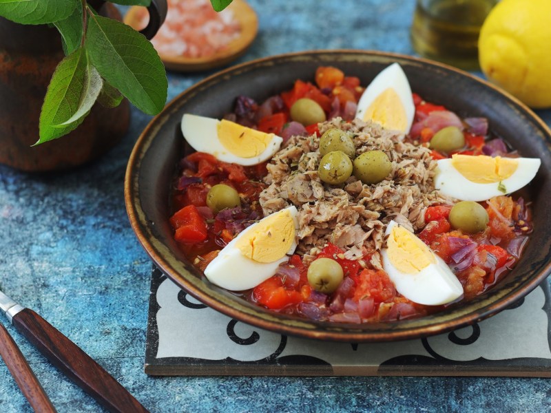 Tunesischer Grillsalat Slata Mechouia, serviert mit Thunfisch und Eiern, auf einem dunklen Teller.