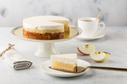 Apfel-Cheesecake auf einem Kuchentablett, davor ein Stück Kuchen.