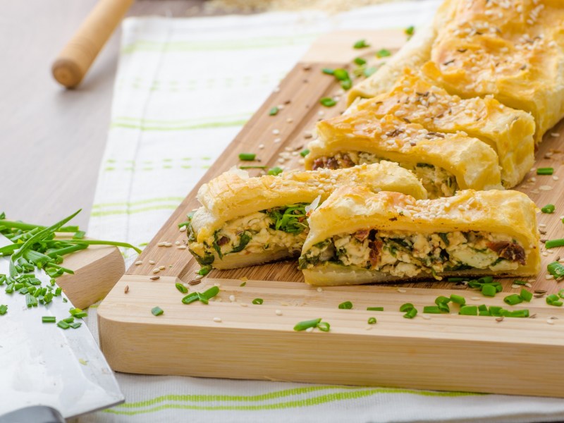 Brett mit angeschnittenem Blätterteigstrudel mit Spinat und Blauschimmelkäse