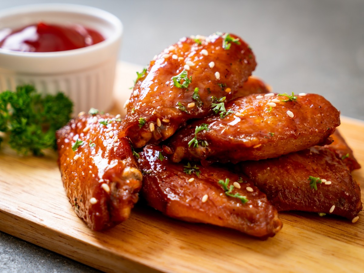 Ein paar Chicken Wings aus dem Airfryer aus einem Brett, bestreut mit Petersilie, daneben eine weiße Schale Ketchup.