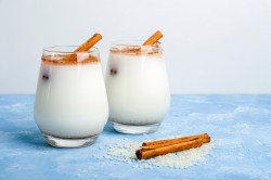 Zwei Gläser Horchata auf einem blauen Tisch, garniert mit Zimt und Zimtstangen.