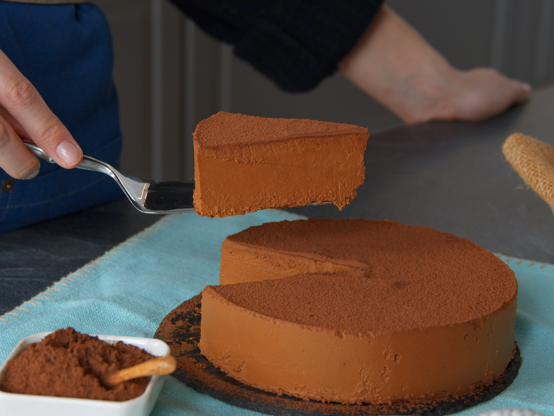 Eine Hand hebt ein Stück Kürbis-Schokokuchen mit einem Tortenheber aus dem restlichen Kuchen.