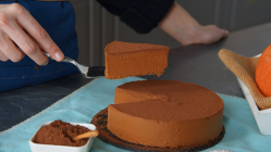 Eine Hand hebt ein Stück Kürbis-Schokokuchen mit einem Tortenheber aus dem restlichen Kuchen.