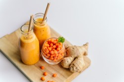 Zwei Gläser Sanddorn-Ingwer-Smoothie mit Sanddornbeeren und Ingwer daneben