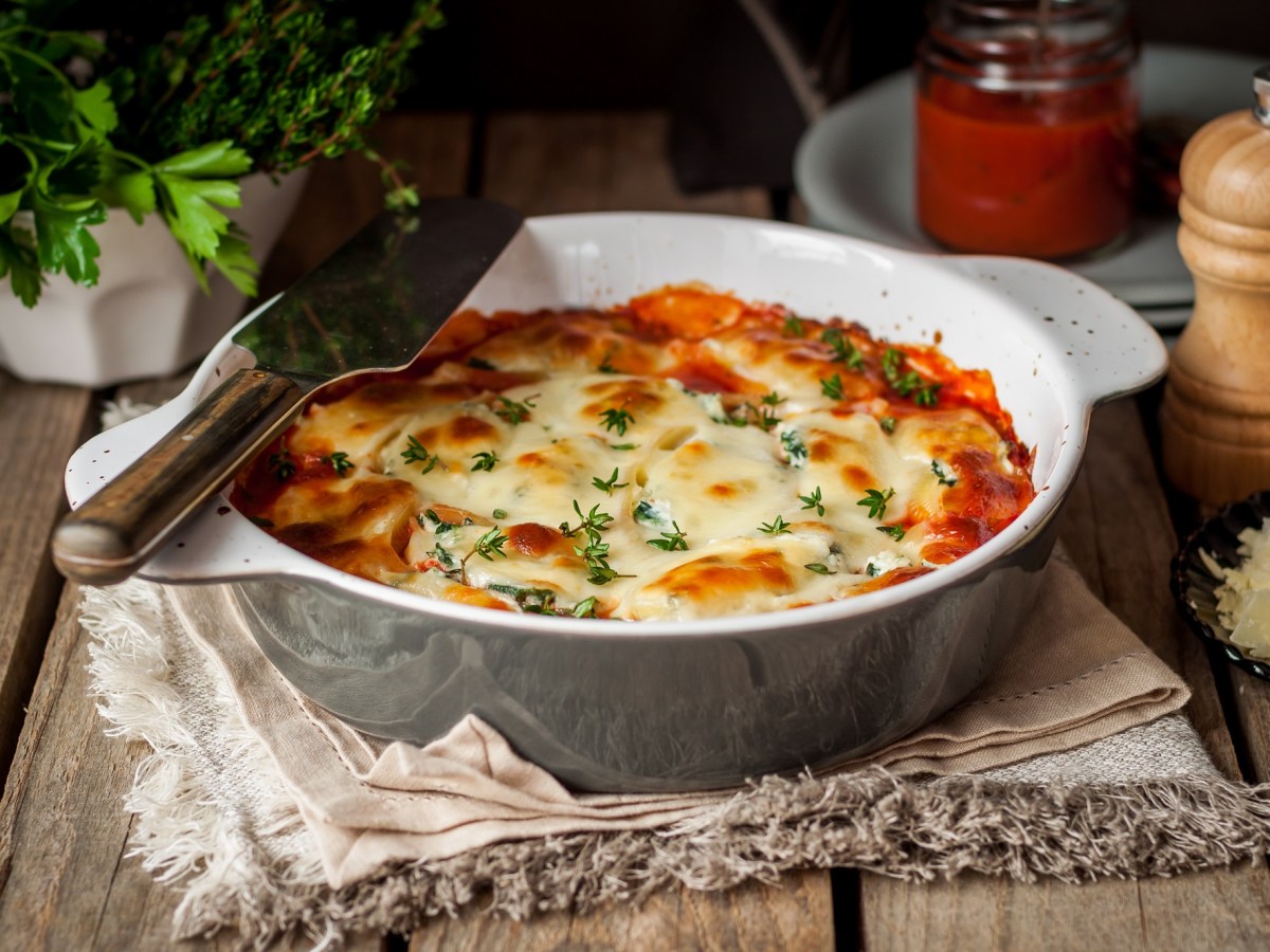 Weißkohl-Lasagne in runder Auflaufform auf einem Geschirrhandtuch, drumherum Gewürzstreuer, und Kräuter.