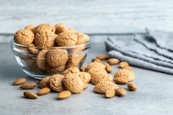 Eine Glasschüssel Amaretti-Kekse, davor einige Kekse und Mandeln.