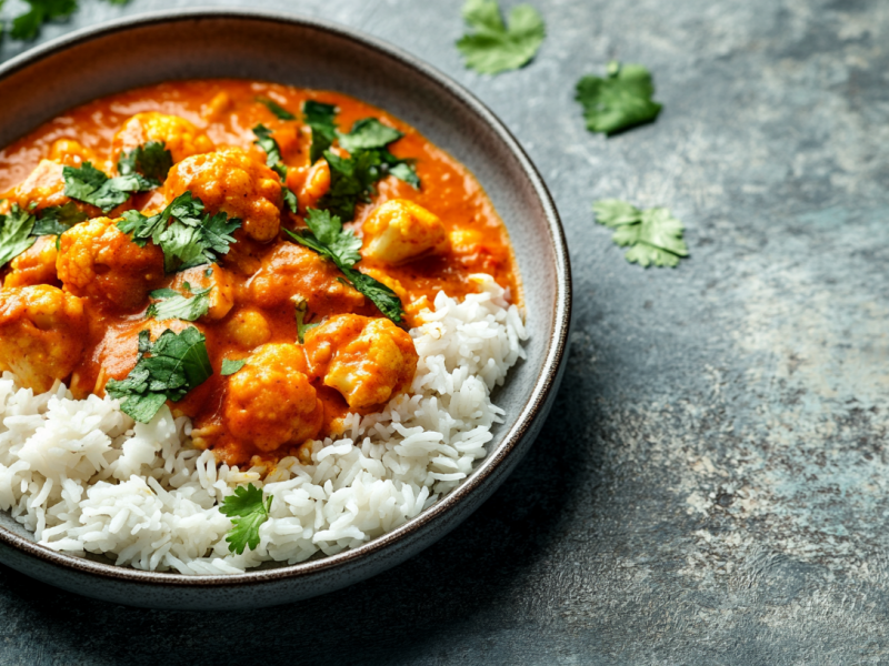 Blumenkohl-Curry aus dem Ofen mit Reis auf einem Teller, bestreut mit Koriander.