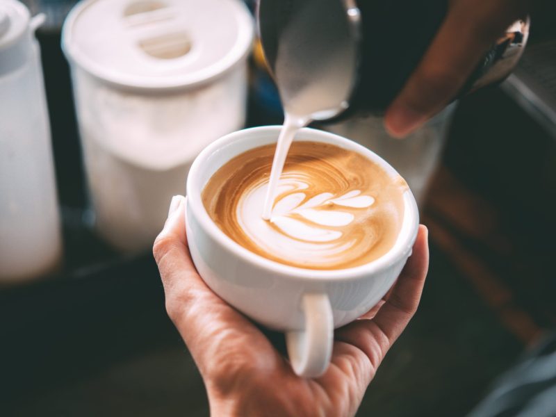 De'Longhi Siebträger im Angebot bei Amazon: Ein Barista kippt Milch in eine Tasse Kaffee.