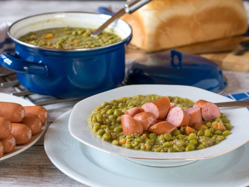 Ein Topf und ein Teller Erbsensuppe mit Würstchen.