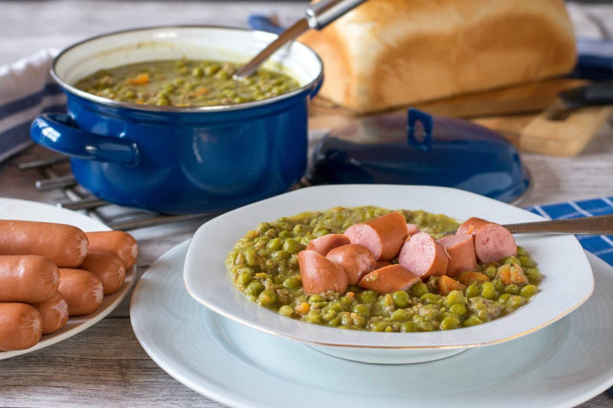 Ein Topf und ein Teller Erbsensuppe mit Würstchen.