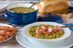 Ein Topf und ein Teller Erbsensuppe mit Würstchen.