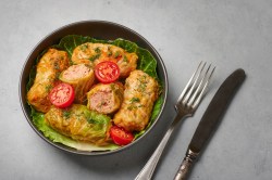 Polnische Kohlrouladen, in einer Schale angerichtet. Garniert sind sie mit halbierten Tomaten.