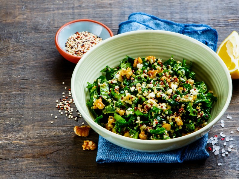 Eine Schüssel Grünkohlsalat mit Feta und Walnüssen, daneben eine angeschnittene Zitrone.