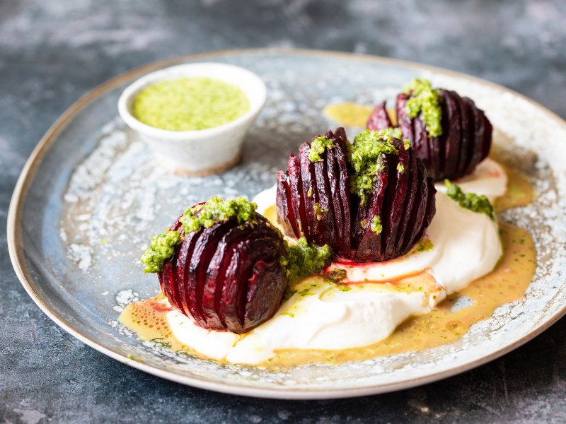 3 Hasselback-Rote-Beten auf einem Teller, garniert mit Kräutersoße und Joghurt.