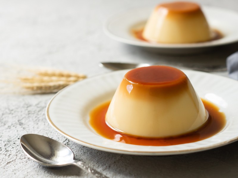 Zwei Karamell-Flan auf je einem kleinen Teller. Drum herum ist Karamellsoße zu sehen.