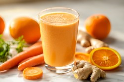 Glas mit Karotten-Ingwer-Smoothie, Orangen, Ingwer und Karotten daneben.