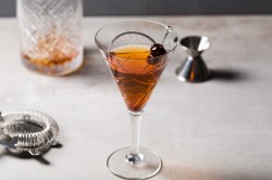 Manhattan-Cocktail, garniert mit Cocktail-Kirschen, in einem gemusterten Glas.