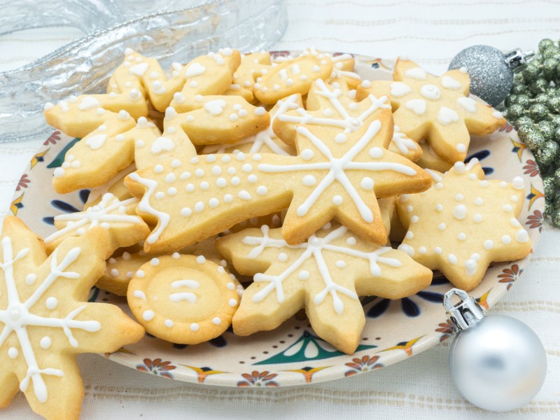 Ein Teller Marzipanplätzchen verziert mit Zuckerguss, daneben Weihnachtsdeko.