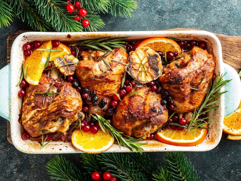 Orangenhähnchen aus dem Ofen in einer Auflaufform, serviert mit Cranberrys und Rosmarin.