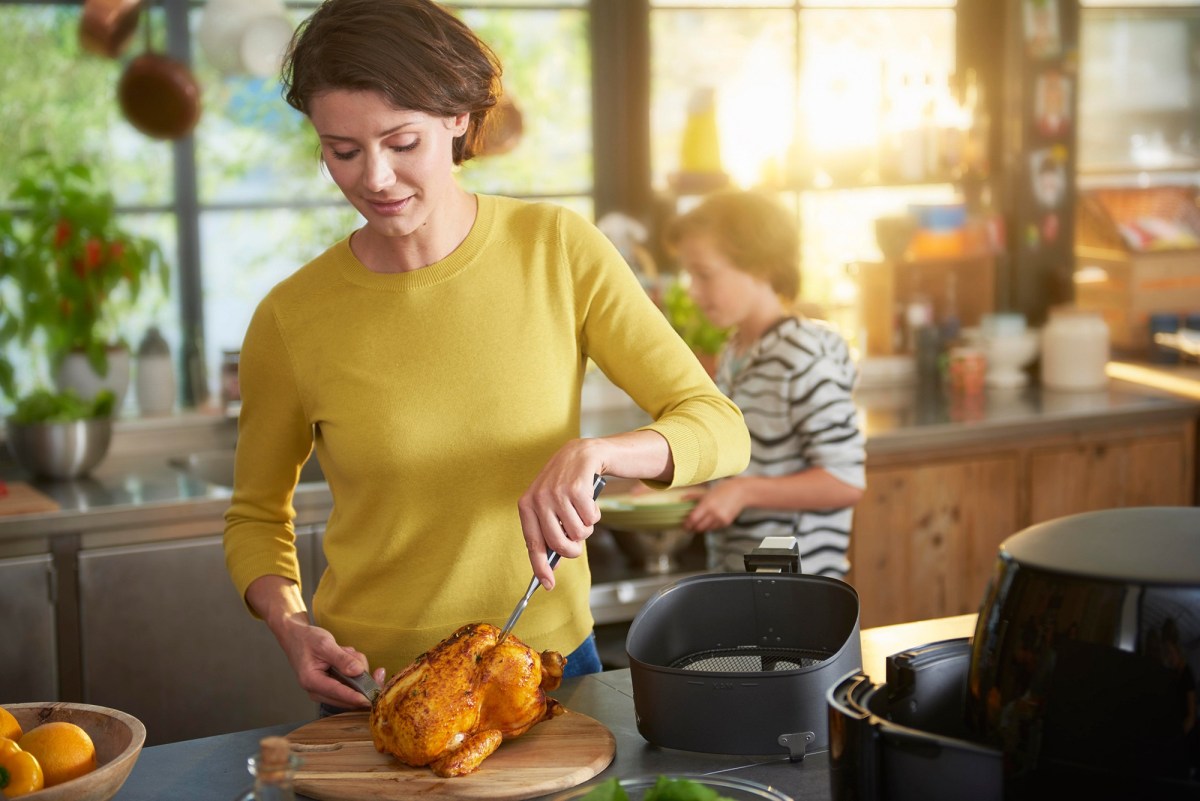 Philips Airfryer XL Black Friday Amazon: Frau kocht mit Heißluftfritteuse ein Huhn.