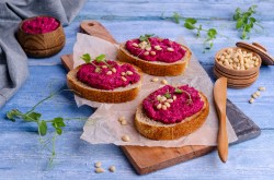 Drei Brotscheiben, mit Rote-Bete-Meerrettich-Aufstrich bestrichen und mit Pinienkernen und Erbsensprossen garniert.