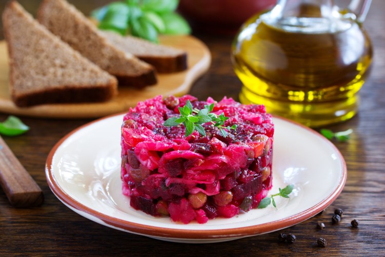 Rote-Bete-Tatar auf einem weißen Teller, dahinter eine Flasche Öl und Brotscheiben.