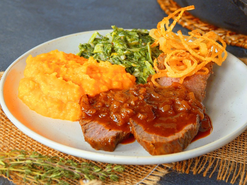 Zwiebelrostbraten mit Kürbispüree und Röstzwiebeln auf einem Teller.