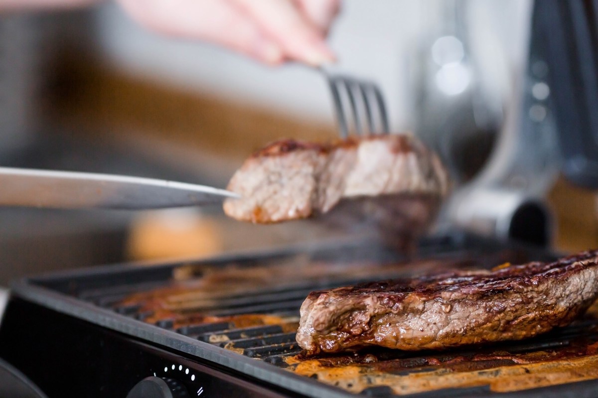 Amazon Black Friday Tefal OptiGrill Kontaktgrill: 2 Stück Fleisch auf einem Kontaktgrill, eins wird mit Messer und Gabel weggenommen. Nahaufnahme.