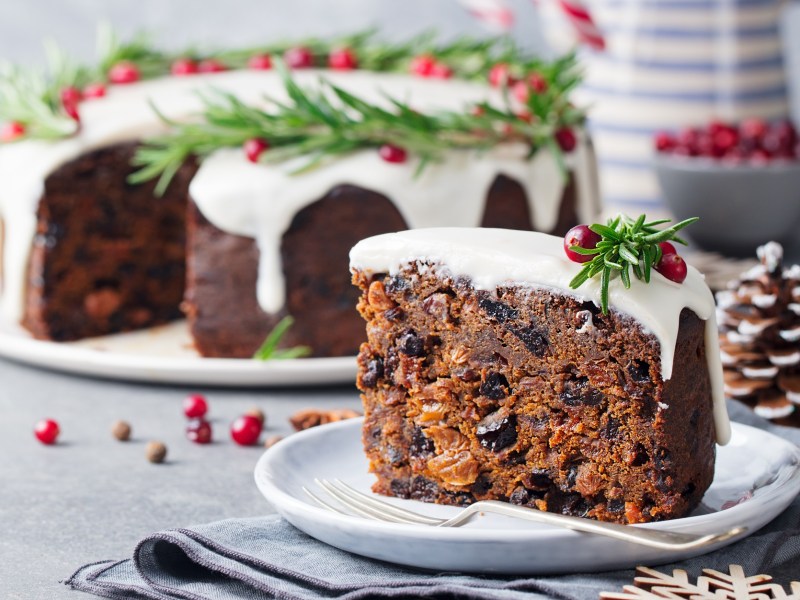 Ein Stück Englischer Weihnachtskuchen. Im Hintergrund ist der Rest des Kuchens zu sehen.