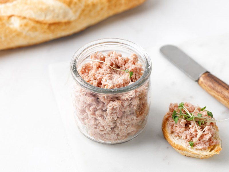 Gänse-Rillettes in einem Glas, einiges davon wurde bereits auf ein Brot gestrichen.