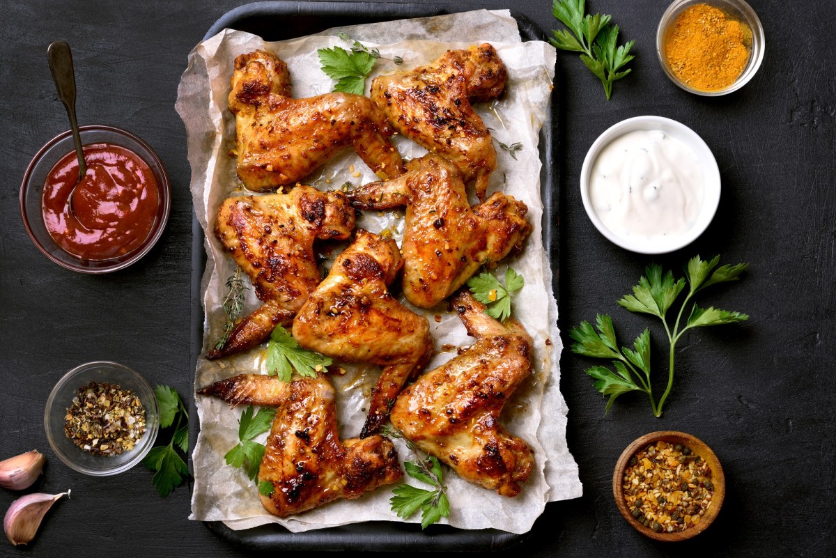 Honig Chicken Wings auf einem mit Backpapier ausgeschlagenen Backblech. Daneben stehen Schüsseln mit Soße.