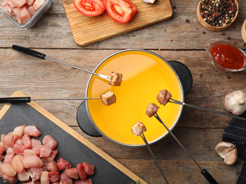 Ein Topf klassisches Fleischfondue, über dem mehrere Fleischgabeln mit Stücken hängen.