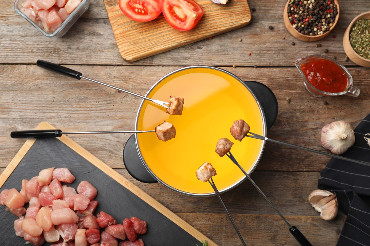 Ein Topf klassisches Fleischfondue, über dem mehrere Fleischgabeln mit Stücken hängen.