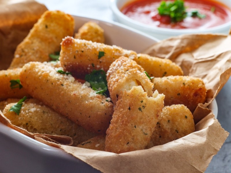 Mozzarella-Sticks aus der Heißluftfritteuse in einer Schale. Daneben ein Schälchen mit Ketchup.