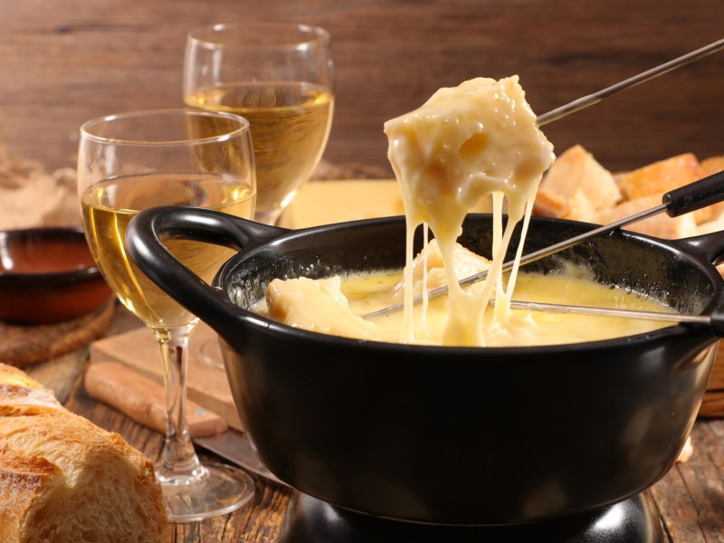 Veganes Käsefondue in einem dunklen Topf, in den Brotstücke an einem Metallspieß getaucht werden.