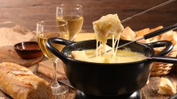 Veganes Käsefondue in einem dunklen Topf, in den Brotstücke an einem Metallspieß getaucht werden.