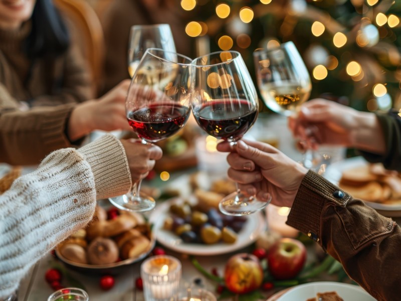 Gemütliche Runde stößt beim Essen mit Wein an.